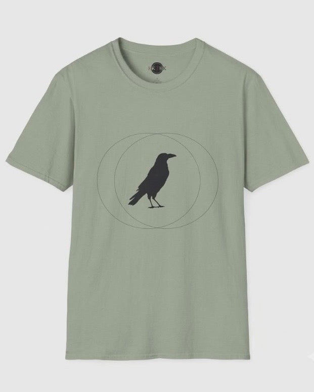 A sage green short-sleeve crewneck t-shirt featuring a black crow silhouette standing inside a geometric circle graphic on the chest, displayed against a light gray background.