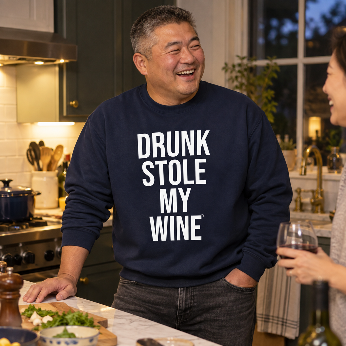 Man wearing a navy Drunk Stole My Wine sweatshirt while preparing dinner