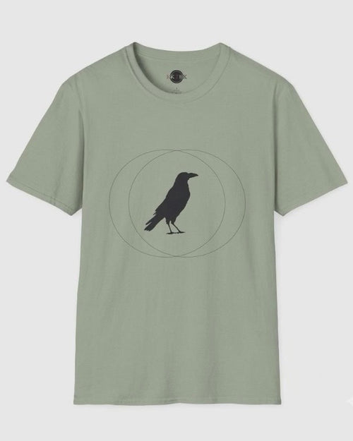 A sage green short-sleeve crewneck t-shirt featuring a black crow silhouette standing inside a geometric circle graphic on the chest, displayed against a light gray background.