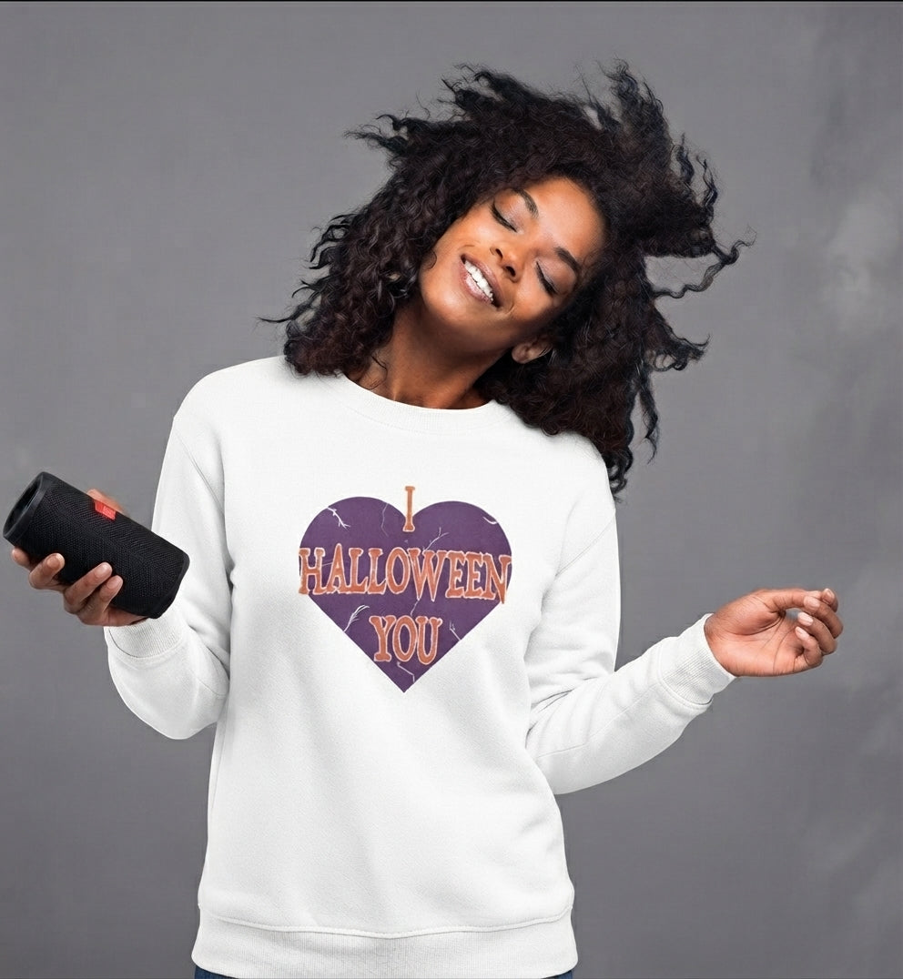 A woman wearing a white sweatshirt with a purple heart graphic that reads 'I HALLOWEEN YOU' in orange letters, holding a black speaker against a gray studio background.