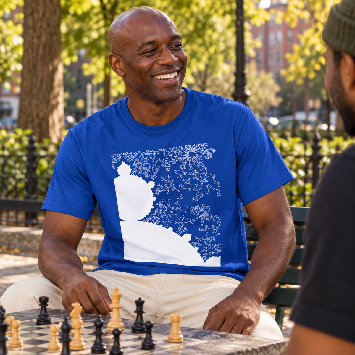 Man wearing a royal blue Mandelbrot Fractal shirt at an outdoor chess table