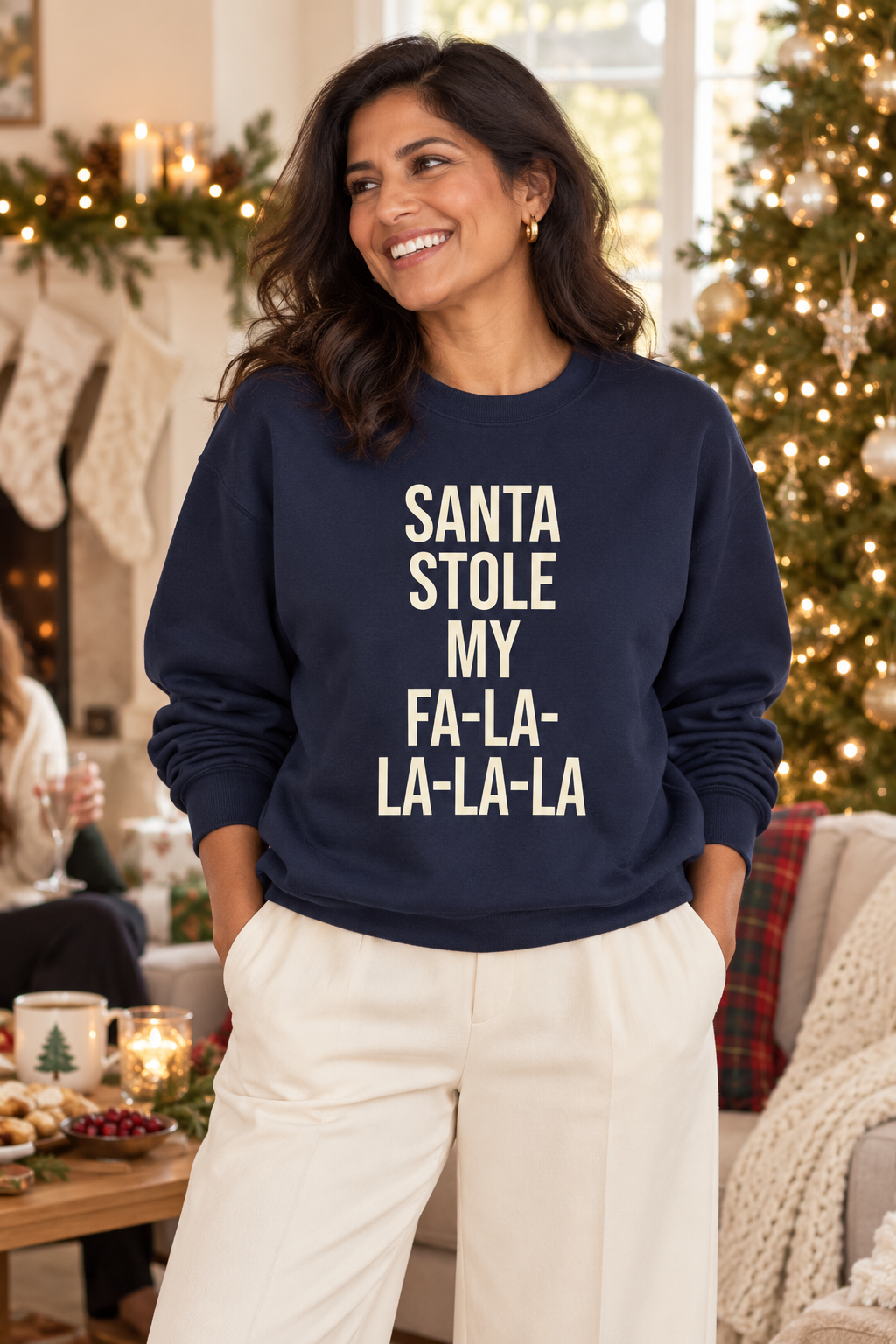 Woman wearing a navy Santa Stole My Fa-La-La-La-La sweatshirt beside a Christmas tree